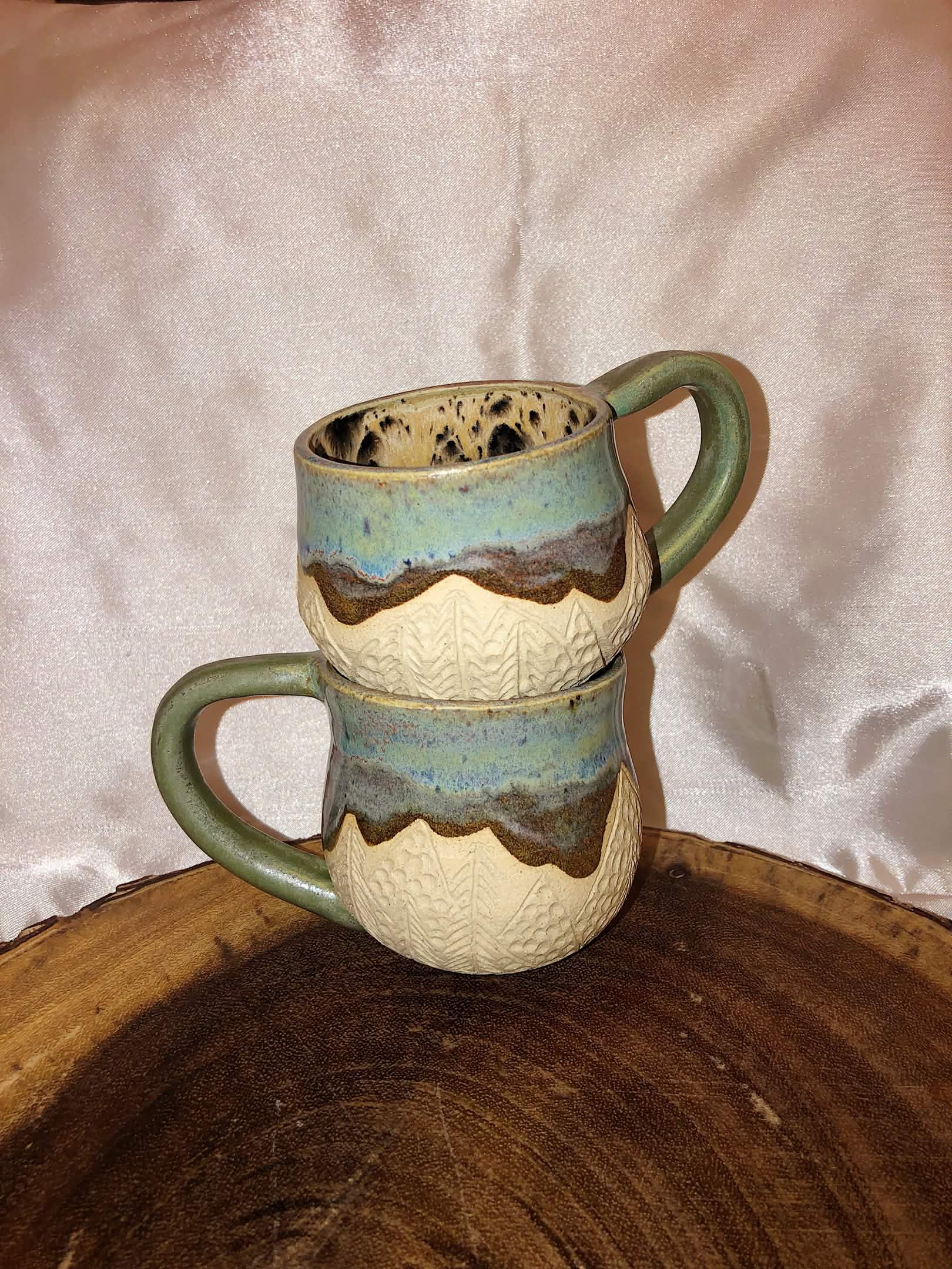 Two mugs with blue + brown glaze and pine tree carvings.